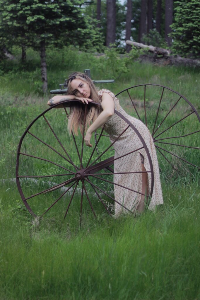 A woman leaning against an old wagon wheel