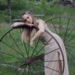 A woman leaning against an old wagon wheel