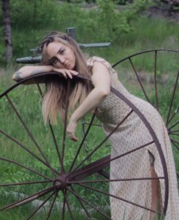 A woman leaning against an old wagon wheel