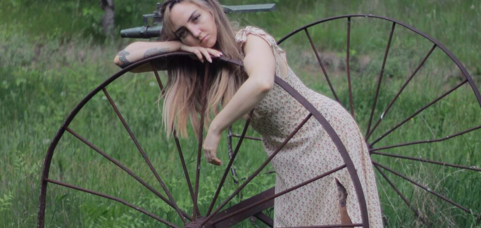 A woman leaning against an old wagon wheel