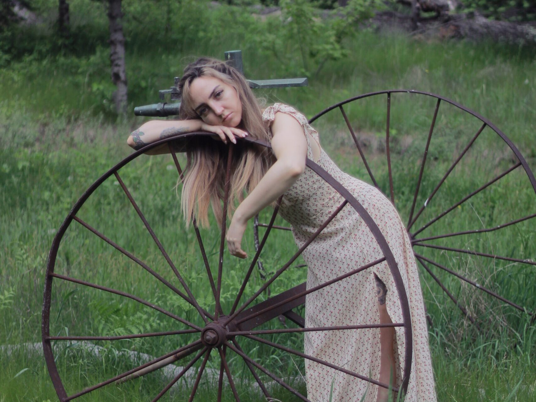A woman leaning against an old wagon wheel