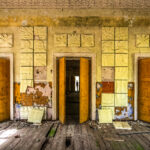 A wall in disrepair with three doors. The center door has a silhouette of a figure at the end of a hallway.