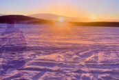 sunset in distance across snow with silouette