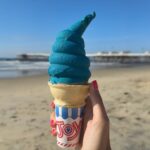 a hand holding a cotton candy ice cream cone at the beach
