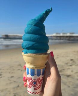 a hand holding a cotton candy ice cream cone at the beach