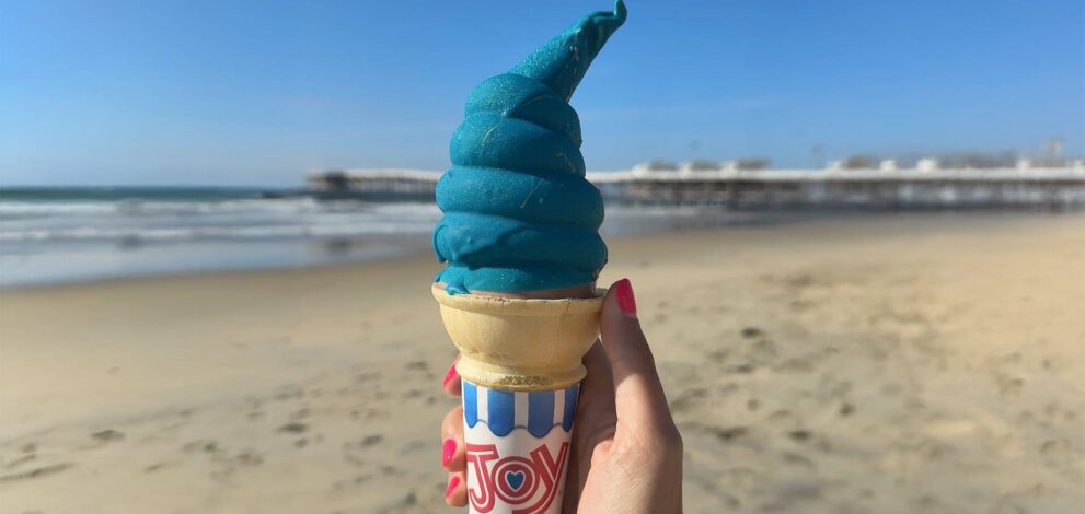 a hand holding a cotton candy ice cream cone at the beach