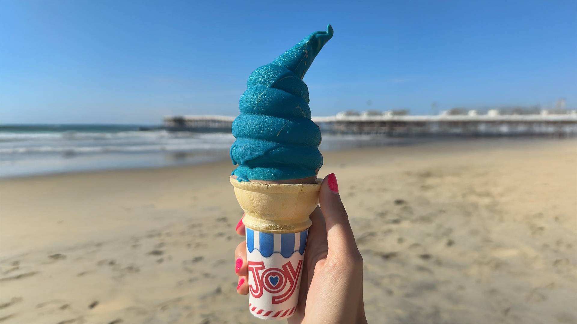 a hand holding a cotton candy ice cream cone at the beach
